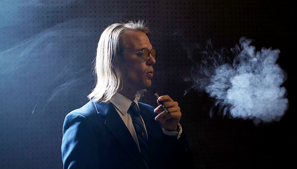 An individual wearing a suit with a white collared shirt and a blue tie. The person is vaping on a THC vape from The Clear cannabis products.