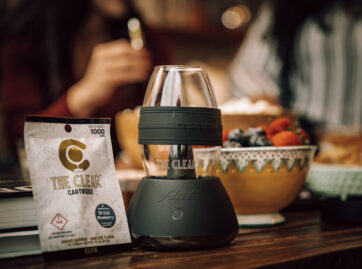 Sitting on a table is The Clear FLÜT Vaporizer. Take a sip from the vapor cup with any 510 thread cartridge. Next to the vaporizer cup is a package for The Clear cartridge. The flavor of the Elite THC vape cart is Blueberry - excellent for nighttime use.