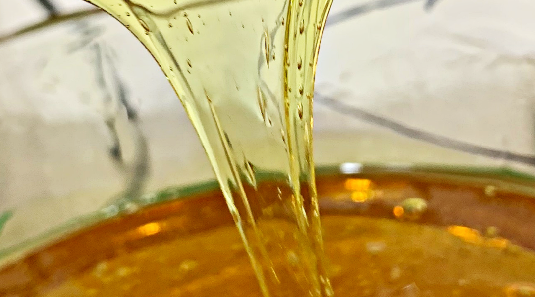 Close up of golden cannabis concentrate being lifted, showcasing the quality of The Clear Cannabis products. The rich color and clarity highlight the purity and excellence of this cannabis extract.