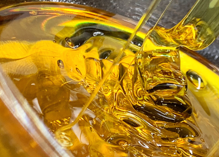 Close up of cannabis concentrate being delicately poured. Produced by The Clear, this premium cannabis product showcases the rich color and quality of their cannabis extracts.