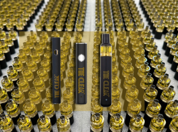 Neatly arranged in clusters are a plethora of cartridges filled with THC distillate. An overlay of The Clear cannabis vape pen batteries can be seen in the center. The vape batteries from left to right are The Clear dual voltage 510 thread battery, The Clear 14mm vape pen battery, and The Clear Elite All-In-One THC Vape.