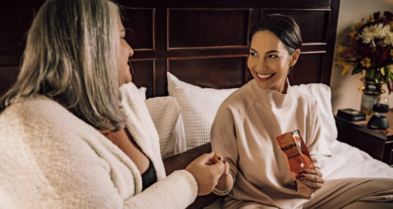 Two women sharing cannabis gummies on a bed